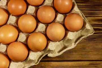 Raw chicken eggs in cardboard pack on wooden table