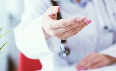 Female doctor making welcome gesture, politely inviting patient to sit down in medical office close-up.