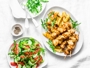 Greek soulvaki with fried potatoes and tomatoes, cucumbers, pepper, arugula salad on a light background, top view