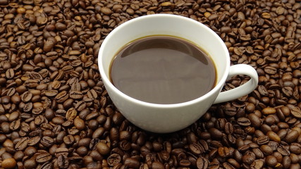 A cup of black coffee over roasted coffee beans