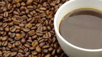 A cup of black coffee over roasted coffee beans