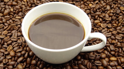 A cup of black coffee over roasted coffee beans