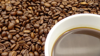 A cup of black coffee over roasted coffee beans