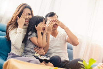 Fototapeta na wymiar happy family mixed race mom dad and daughter enjoy watching tv show or game play together weekend activity home background