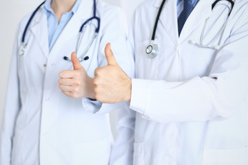 Team of unknown medicine doctors showing OK sign with thumb up close up. Success and high level service in health care, best treatment and customer loyalty and physical concept