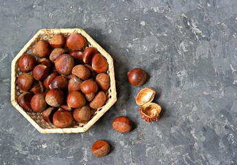 Raw edible chestnuts in a wicker basket on a dark gray concrete background. Top view, copy space.