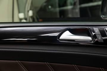 Obraz na płótnie Canvas A close-up view of a part of the interior of a modern luxury car with a view of a silver-colored door handle on a chrome finish with black wood trim