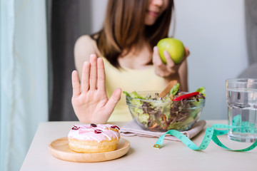Young healthy woman using hand push out dessert and sweets and choose green apple and fresh salad,...