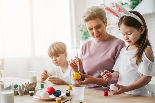 Beautiful grandmother and her granddaughter painting Easter eggs at home