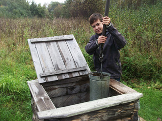 Boy collects water in a bucket from a well