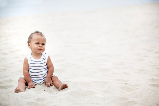 Cute little boy sitting in the sand on the beach playing in the sand. Candid photo of a mixed race child on vacation with lots of copy space