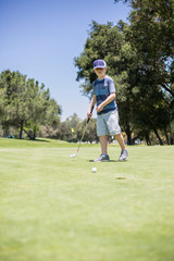 Fototapeta premium A young boy putting a golf ball on the green while playing golf. Vertical photo of a child learning the game of golf