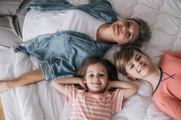 Top view of happy children and their grandmother lying on bed