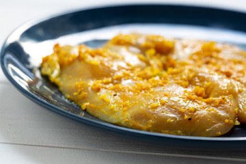 Raw, flavored with turmeric, basil and oregano chicken fillet on a plate.