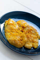 Raw, flavored with turmeric, basil and oregano chicken fillet on a plate.