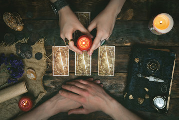 Tarot cards, magic book and fortune teller hands on a wooden table background. Future reading concept. Divination.