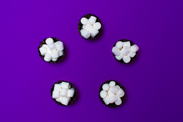 marshmallows in the forms for cakes on a purple background, five pieces. Arranged in a circle. View from above.