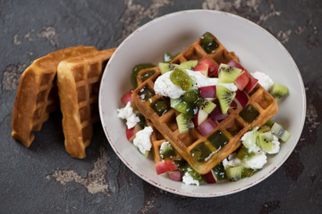 Plate with belgian waffles, fresh fruits and ricotta cheese, studio shot on a brown stone background