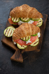 Croissants with red fish, grilled zucchini and ricotta cheese on a dark brown stone background