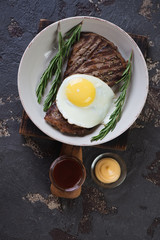 Plate with grilled beef schnitzels and fried egg, above view on a brown stone background
