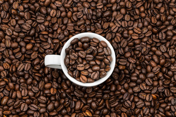 White ceramic cup full of roasted coffee beans on the coffee beans background