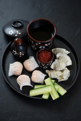 Metal serving tray with steamed dim-sum dumplings and wontons, vertical shot on a black stone surface