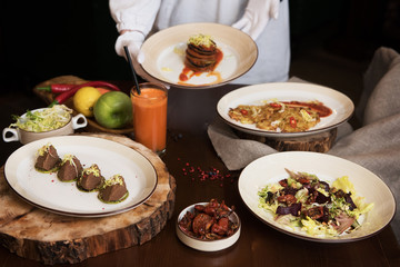 Healthy vegeterian food on brown wood board. The waitress brings food. Salad from beet with dried tomatoes and cabbage, potato vegan pancakes, dried tomatoes, pate from red beans, baked vegetables in