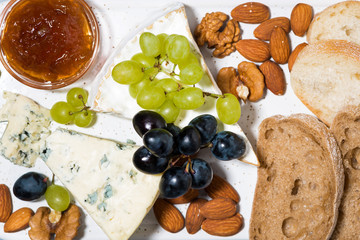 delicatessen cheeses on the board, fresh ciabatta, grapes and jams, closeup top view