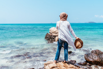 Back view of young asian woman looking from stone. Future and research concept. woman left hands up standing on cliff over sea. Travel mood, concepts of winner, freedom, 