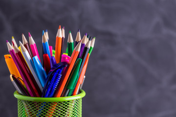 Pens and pencils in metal holder in front of wall background
