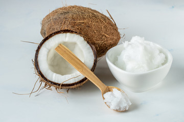 Coconut oil in a jar and coconut halves on the table on a white background