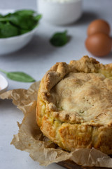 Spinach, chicken and ricotta pie with fresh spinach leaves, ricotta and eggs on a light stone background.