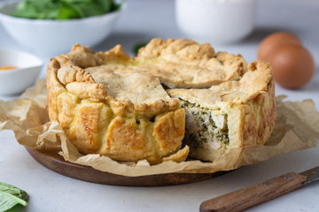 Spinach, chicken and ricotta pie with fresh spinach leaves, ricotta and eggs on a light stone background.
