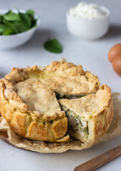 Spinach, chicken and ricotta pie with fresh spinach leaves, ricotta and eggs on a light stone background.