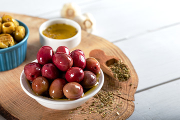 Green and red olives in bowl with olive oil and spices on wooden background