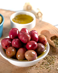 Green and red olives in bowl with olive oil and spices on wooden background