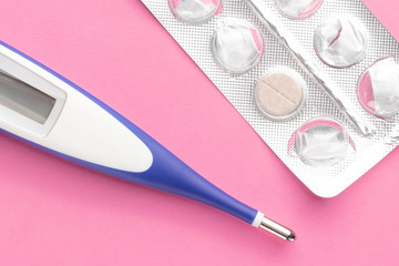 Electronic thermometer and packaging of tablets on a pink background.