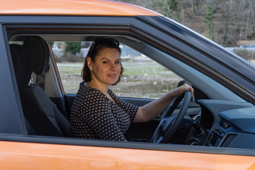 Happy woman sitting behind the wheel of a car smiling and looking at camera