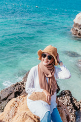 Young confident muslim woman white dress catching a hat on seashore. Travel Vacation Retirement Lifestyle Concept. asian woman wear sun glass looking on the beach in vacation day. summer time.