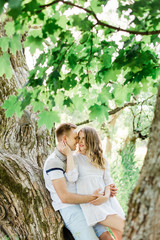 Young pretty couple in love lying on tree in park. Handsome cheerful blonde girl in white dress hugging her boyfriend. Man and woman having fun outdoors