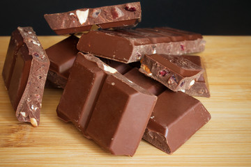 pieces of chocolate with almonds, raspberries and cranberries on a wooden Board with a black background