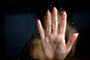 Female hand palm silhouette behind the window with raindrops reaching for the glass. A request for help, depression, stress blurred bokeh background. Refusal  denial of alcohol and drugs
