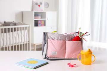 Maternity bag with baby accessories on table indoors. Space for text