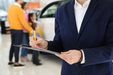 Car salesman with clipboard and blurred family on background