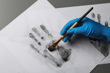 Detective taking fingerprints with brush from paper on grey background, top view.  Criminal investigation