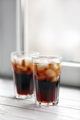 Glasses of cola with ice near window, space for text