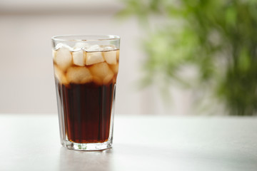 Glass of cola with ice on table against blurred background, space for text