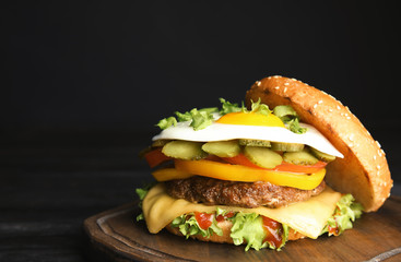 Tasty burger with fried egg on board against dark background, space for text