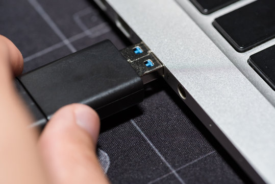 Hand inserting USB flash memory drive plugged into a computer laptop port.