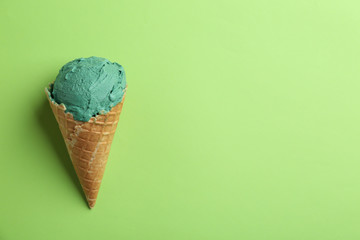 Delicious spirulina ice cream in waffle cone on color background, top view. Space for text